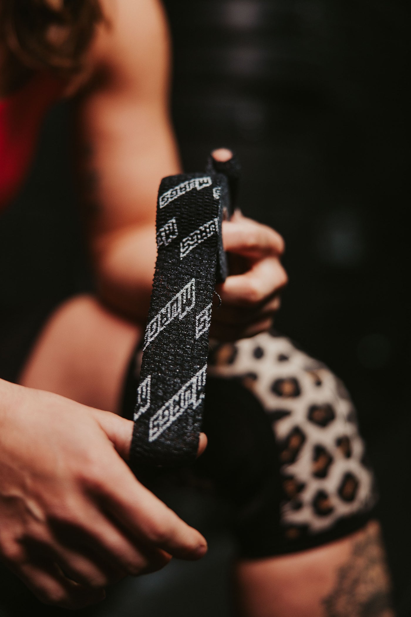 A visual demonstration of the advantages thumb tape provides for weightlifters. This scenario features two weightlifters, one Caucasian female and one African American male, practicing at a gym. Both 